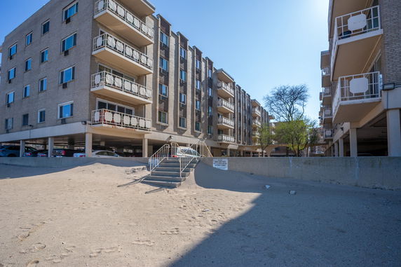 Front view of a multi-story residential building with balconies and covered parking at ground level.