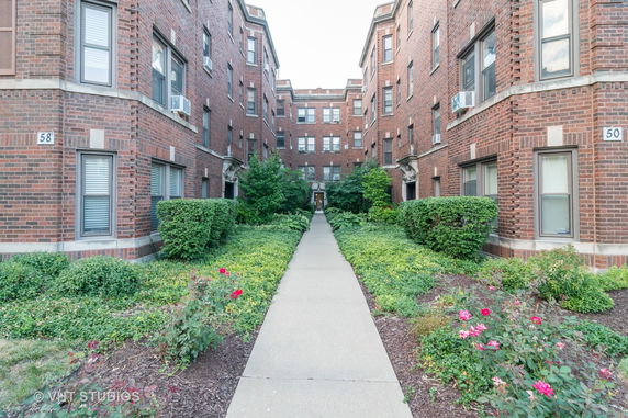 Front view of a brick residential building with a central walkway and greenery.