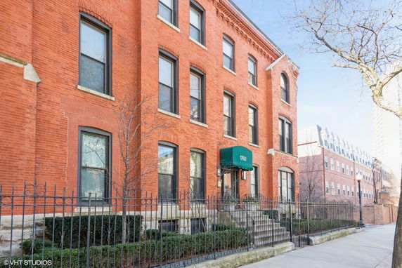Front view of a multi-story brick building with an arched entrance and green awning.