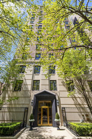 Front view of a multi-story building with large windows and ornamental plants by the entrance.