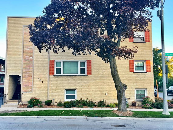 Front view of a two-story brick building with several windows and a tree in front.