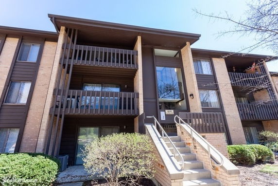 Front view of a multi-story apartment building with balconies and an entrance staircase.
