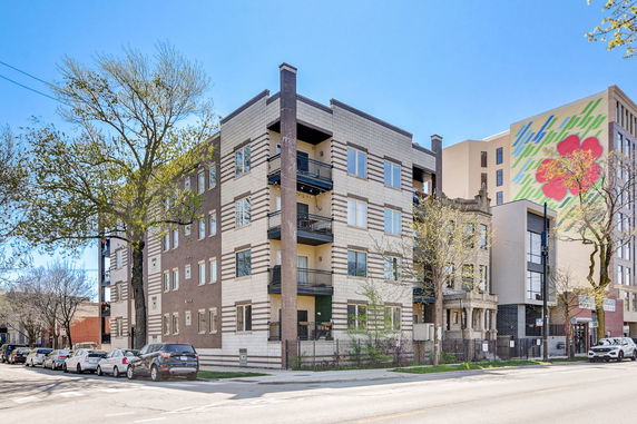 Front view of a multi-story apartment building with balconies and brick facade.