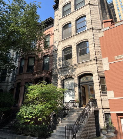 Front view of a multi-story stone townhouse with stairs leading to the entrance.