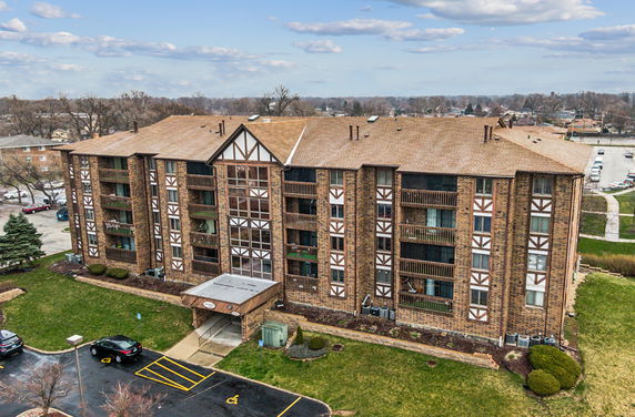 Front view of a multi-story brick apartment building with a gabled roof and balconies.