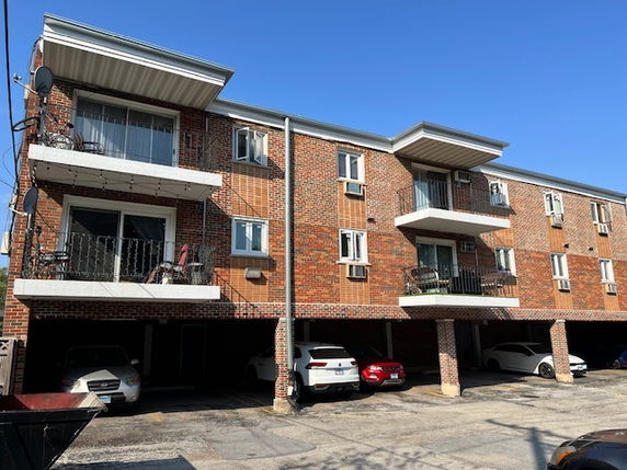 Front view of a multi-story brick apartment building with balconies and under-building parking.