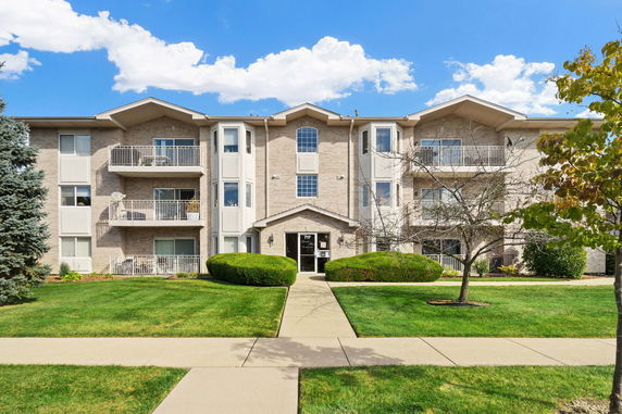 Front view of a three-story residential building with balconies and brick facade.