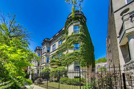 Front view of a multi-story building covered with ivy and surrounded by a black metal fence.