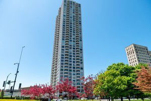 Front view of a tall residential building with multiple balconies against a clear blue sky.