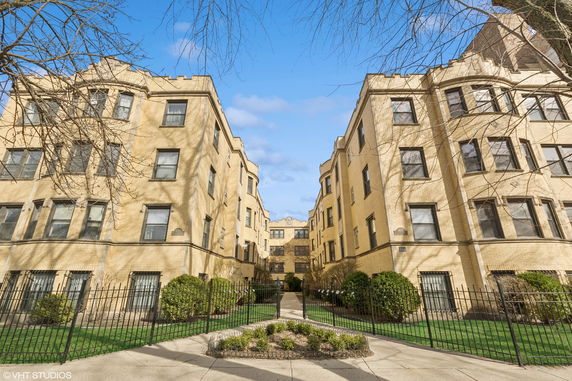 Front view of a multi-story apartment building with a central pathway and fenced garden.