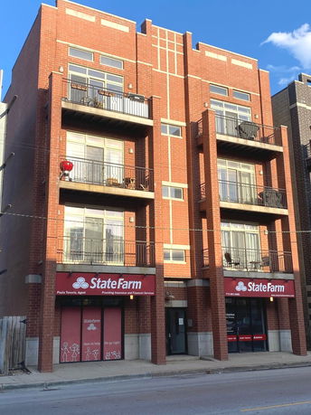 Front view of a multi-story brick building with balconies and a State Farm office on the ground floor.