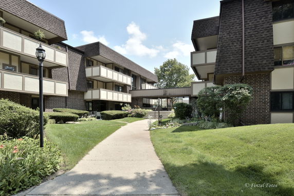 Front view of a multi-story residential building with balconies and a landscaped pathway.