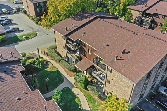 Aerial view of a residential building complex with surrounding greenery and parking area.