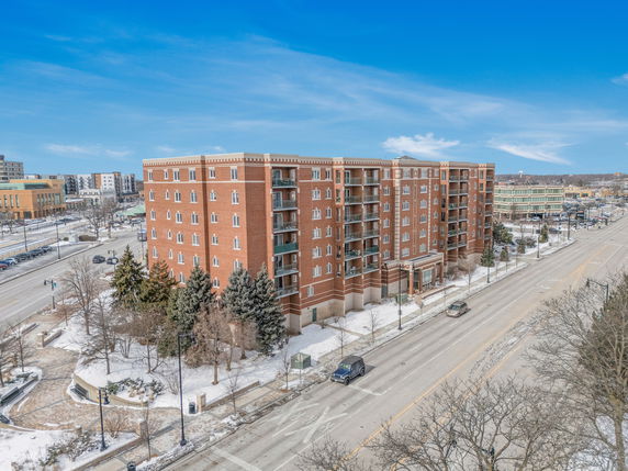 Front view of a multi-story brick building with balconies, situated along a snowy street.