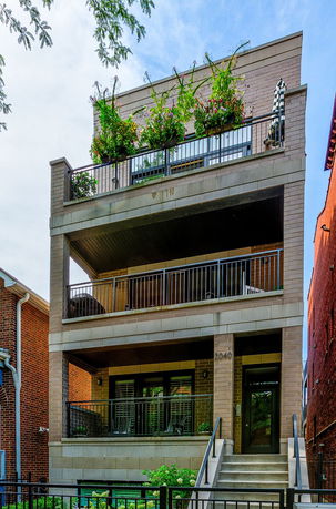 Front view of a three-story building with balconies and greenery.