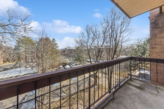 View from a balcony overlooking trees and a parking area.