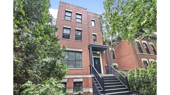 Front view of a three-story brick house with a black entrance staircase.