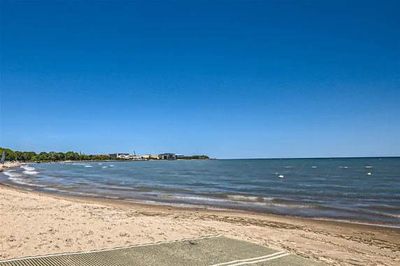 Wide view of a beach with ocean and buildings in the distance.