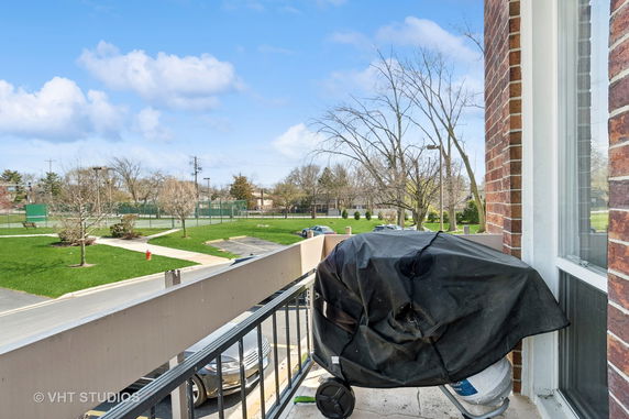 View from a balcony showing a tennis court and a grassy area with trees.