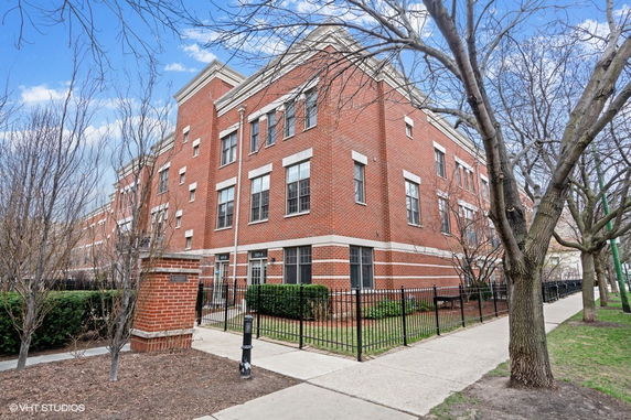 Front view of a multi-story brick building with multiple windows and a fenced perimeter.