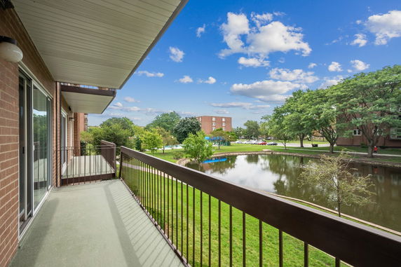View from a balcony showing a pond, trees, and a distant building.