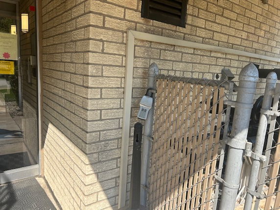 Exterior view of a brick building corner with a metal and wooden gate.