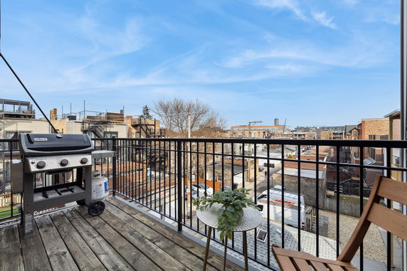Outdoor balcony view with grill and table overlooking urban surroundings.