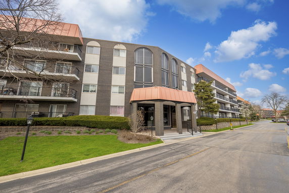 Front view of a multi-story apartment building with balconies and an entrance canopy.