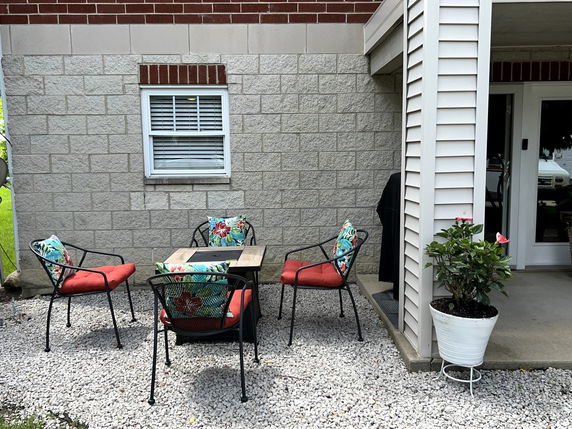 Outdoor seating area with colorful chairs and table against a brick and siding house exterior.