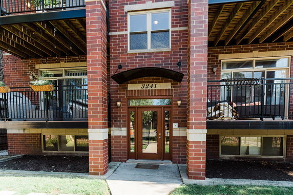 Front view of a multi-story brick building with balconies and an entrance door.