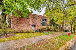 Front view of a brick house with large windows and surrounding trees.