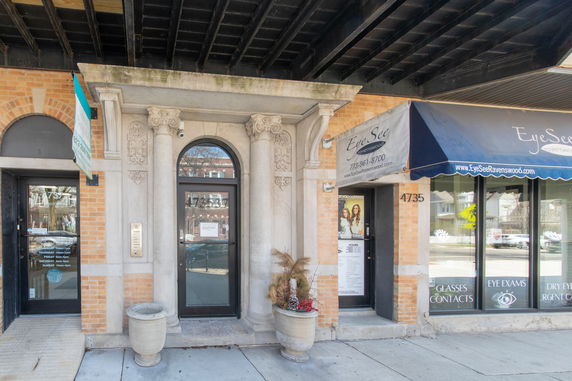 Front view of a building entrance with ornate columns and a shop with an awning.