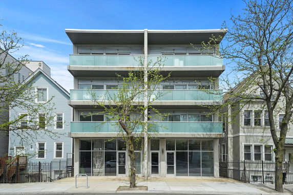 Front view of a modern multi-story building with glass balconies and a flat roof.