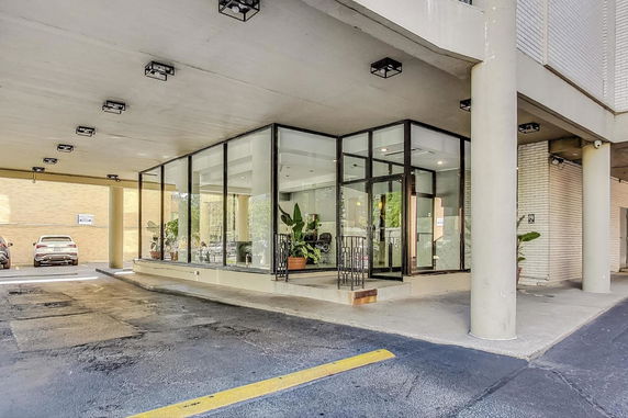 Covered parking area with glass-walled entrance to a building.