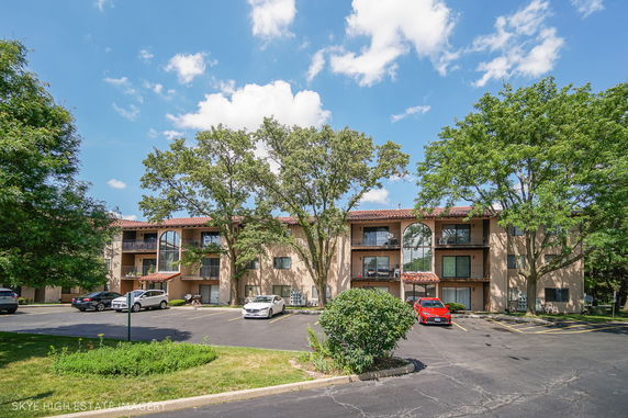 Front view of a multi-story residential building with balconies and a parking area.