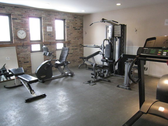 Room with gym equipment including a treadmill and weight machines.