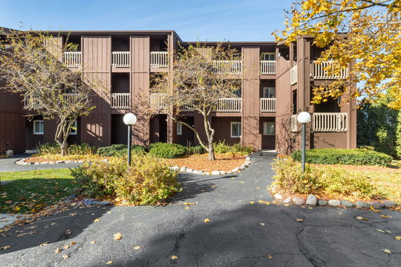 Front view of a three-story building with balconies and surrounding trees.