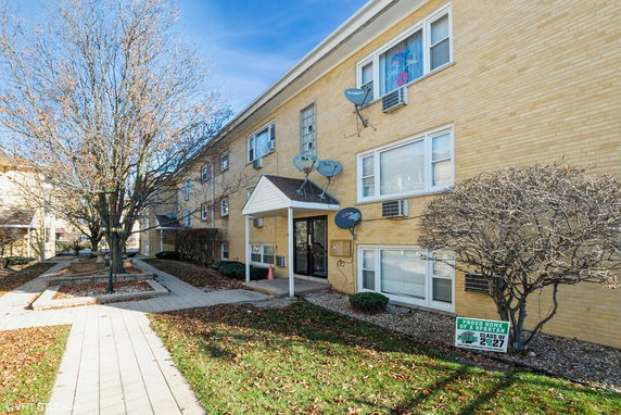 Front view of a multi-story apartment building with brick exterior and multiple satellite dishes.