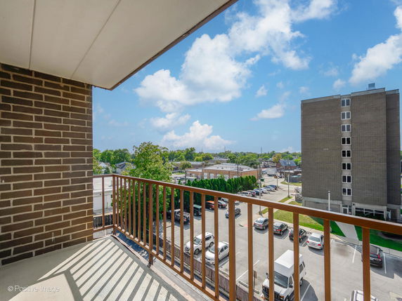 View from a balcony overlooking a parking area and distant buildings.