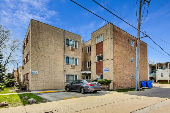 Front view of a multi-story apartment building with brick exterior and parking area.