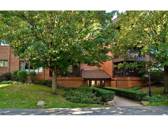 Front view of a multi-story brick building with balconies and surrounded by trees.