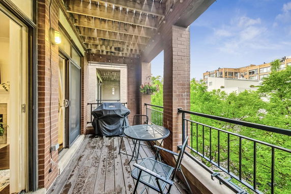 Balcony with outdoor furniture and grill, offering a view of nearby buildings and greenery.