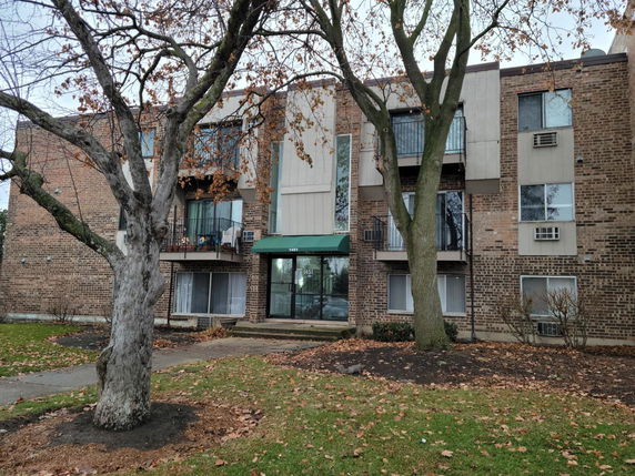 Front view of a multi-story apartment building with brick facade and small balconies.
