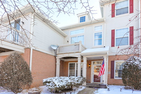 Front view of a house with a small balcony, brick and siding exterior, and a front entrance featuring an American flag.