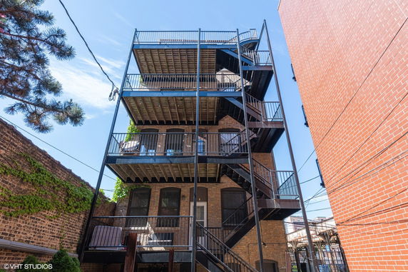 Exterior view of a multi-story building with balconies and metal staircase.