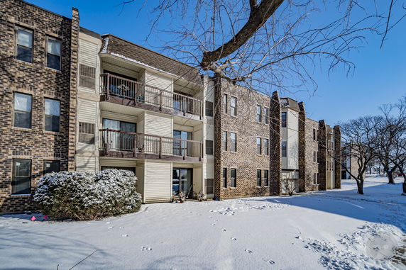 Front view of a multi-story building with brick facade and balconies, surrounded by snow.