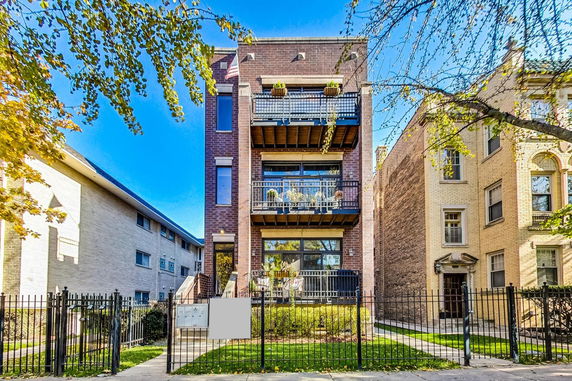 Front view of a multi-story brick building with balconies and metal railing.
