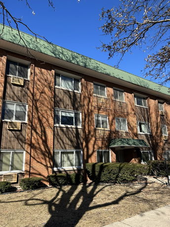 Front view of a multi-story brick building with multiple windows and a green roof.