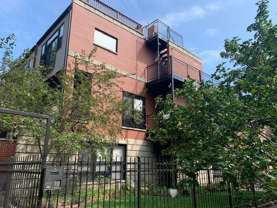 Front view of a multi-story brick building with external staircase and rooftop railings.