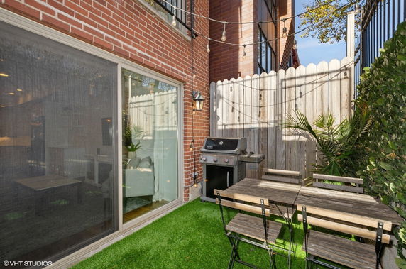 Outdoor patio area with brick walls, sliding glass door, barbecue grill, and wooden table with chairs.